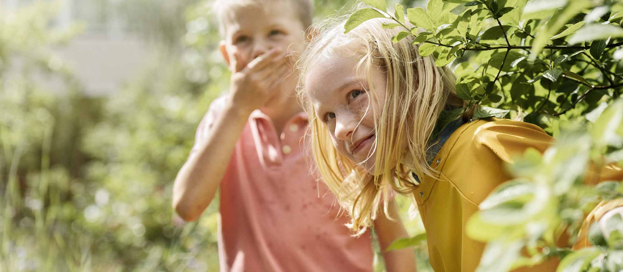 Två barn gömmer sig bakom en buske i trädgården